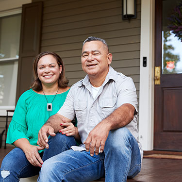Older couple sitting on stoop in front of house with Slomins doorbell camera and Personal emergency pendant